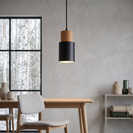 Black cylinder pendant with a wood top hanging beside a dining table