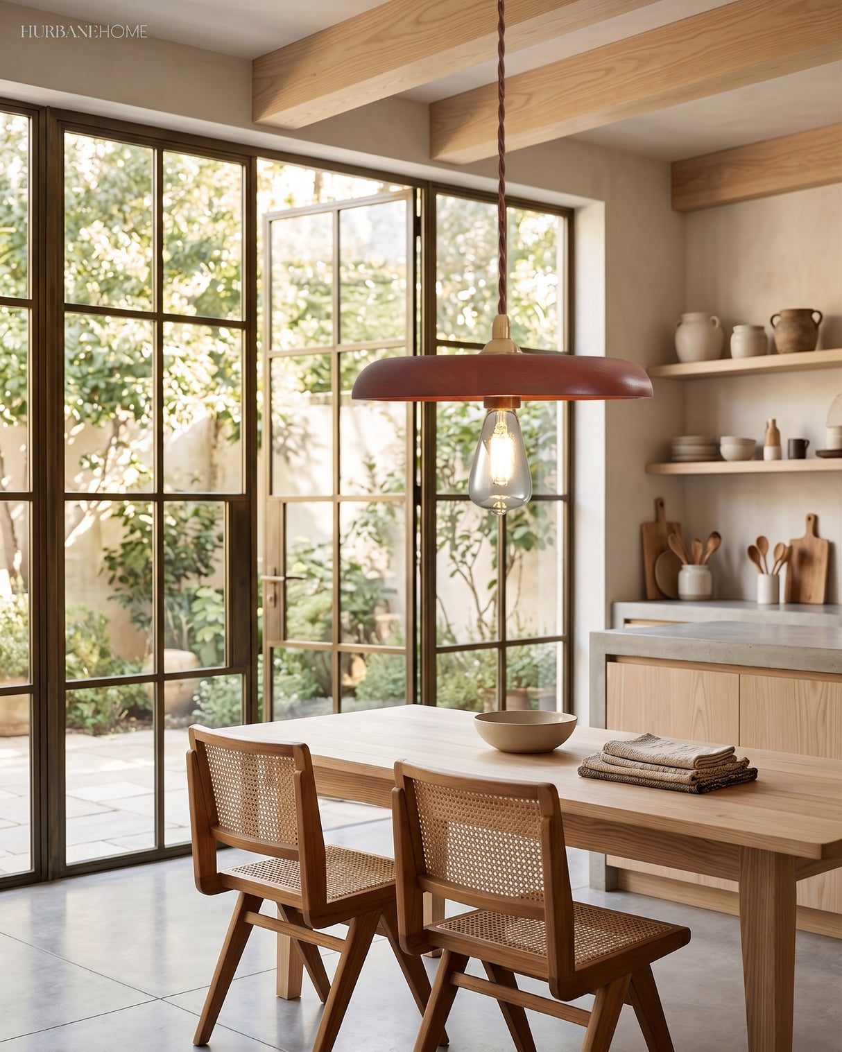 Walnut wood disc pendant lit above a light timber dining table by glass doors