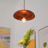 Wood pendant lit in a white hallway above framed prints and a vase of foliage