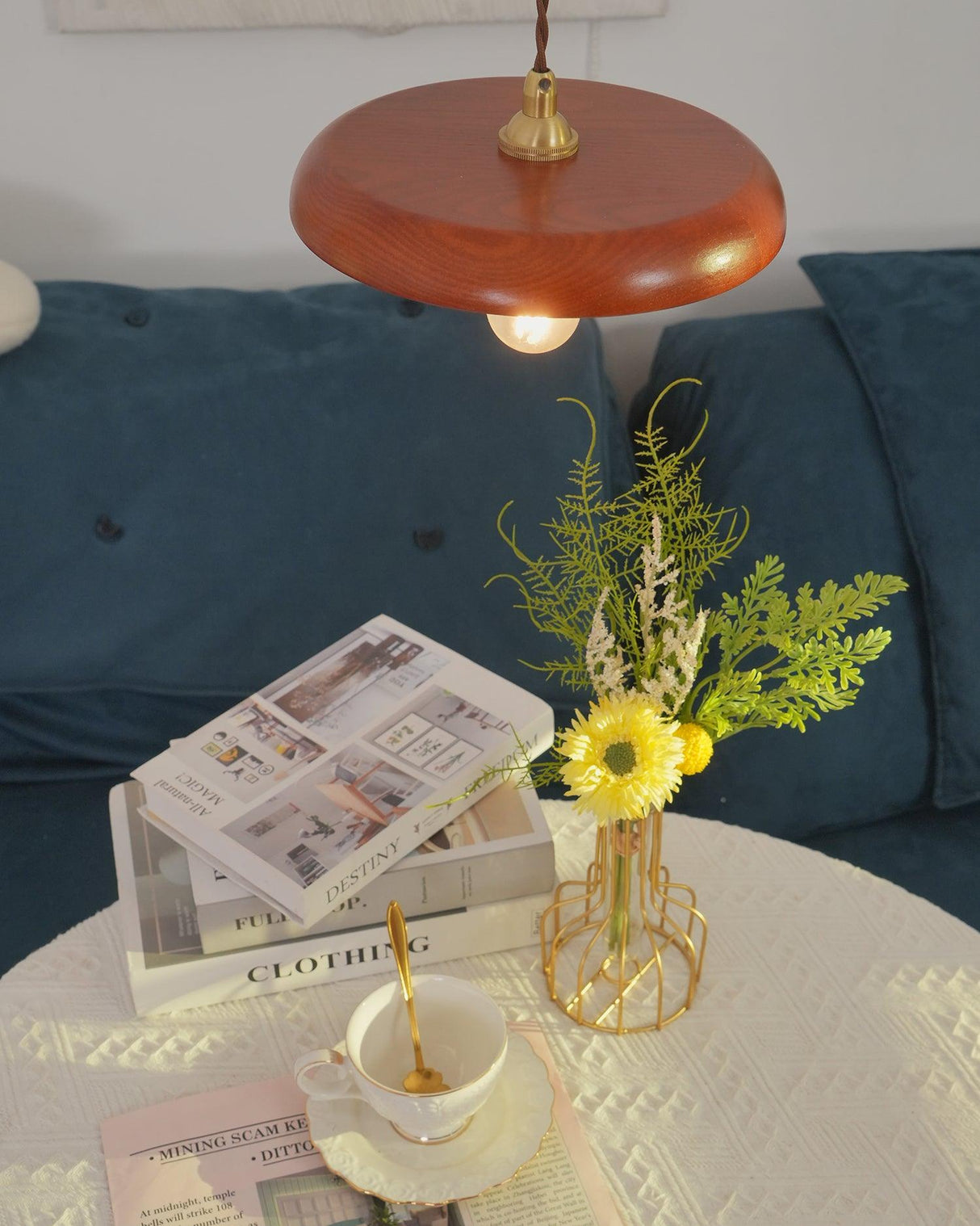 Wood pendant above a side table with a newspaper, cup and dried flowers