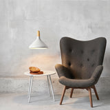 White pendant with a wood collar lighting a side table beside a grey armchair