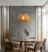 Wood slat pendant above a round dining table beside window blinds