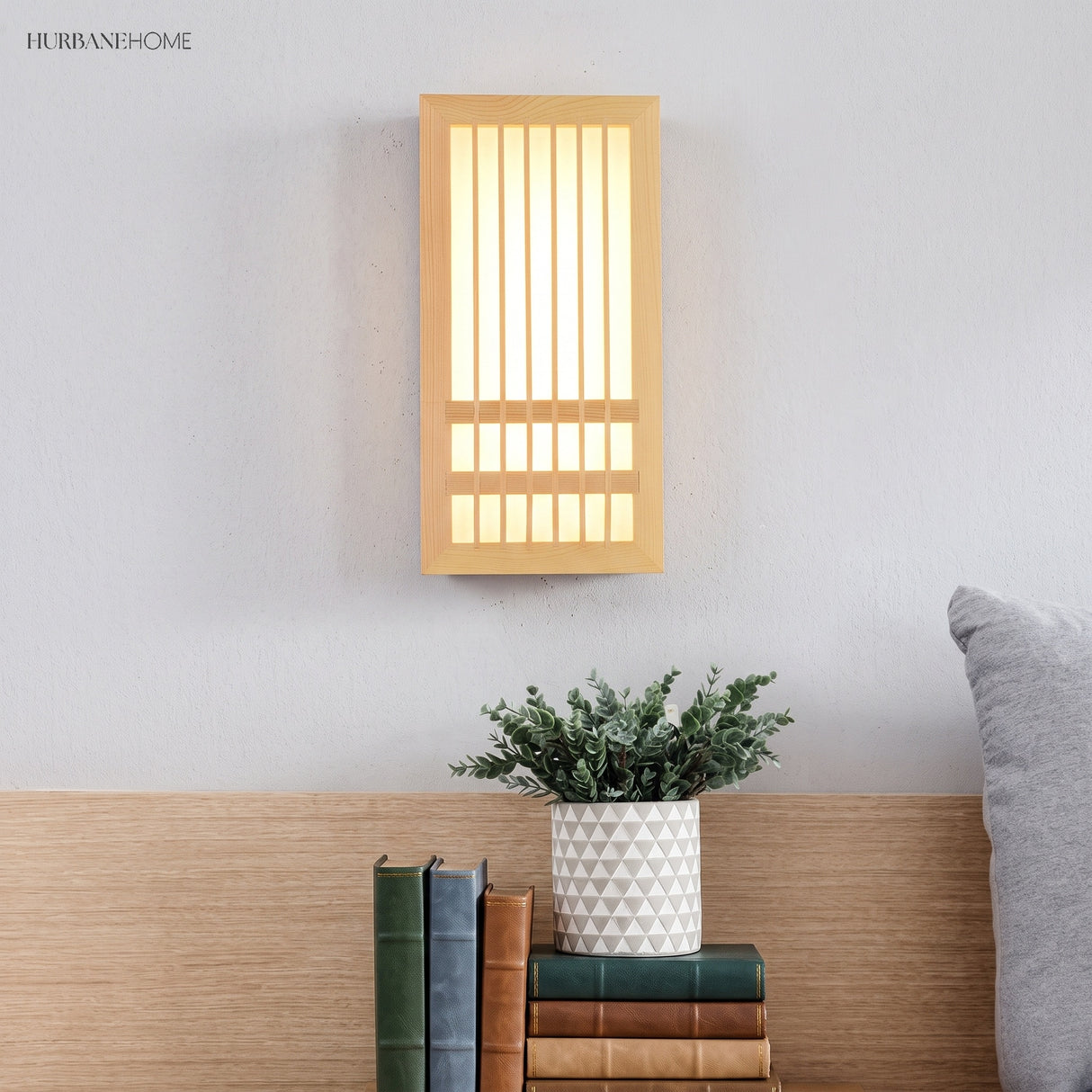 Wood wall sconce lit above a headboard with books and a potted plant below