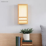 Wood wall sconce lit above a headboard with books and a potted plant below