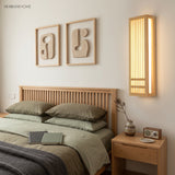 Natural wood wall sconce lighting a bedroom beside framed art and a nightstand