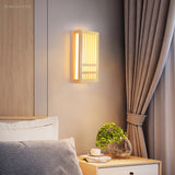 Small wood wall sconce casting a warm glow beside a bed and nightstand