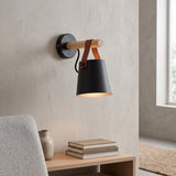 Black shade sconce on a wooden arm beside a chair and window