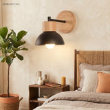 Wood sconce with a black dome lit beside a bed and potted plant