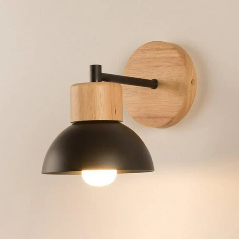 Wood sconce with a black dome lit against a pale studio wall