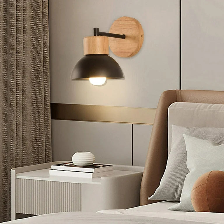 Black domed wood sconce lit above a bedside table and lamp