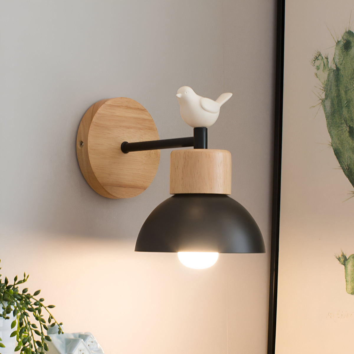 Wood sconce with a black dome and bird lit beside a cactus print