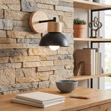 Wood and black iron dome sconce lit above a desk against stone