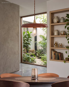 Wood pendant light hanging over a small round table beside a planted courtyard