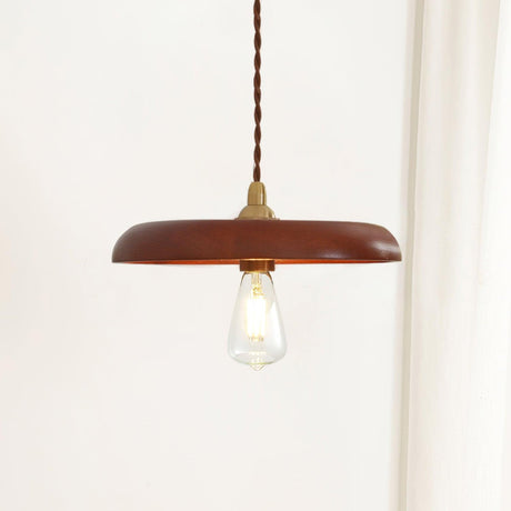Wood disc pendant with a lit filament bulb hanging beside a white curtain
