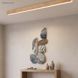 Light wood tone linear ceiling light above a console and stone art