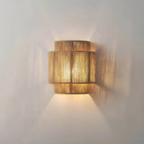 Woven rope wall lamp lit, throwing light up and down a pale wall