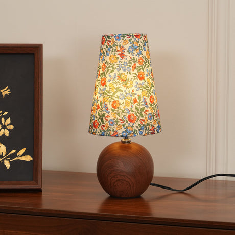 Yellow floral shade table lamp lit on a sideboard with a botanical print