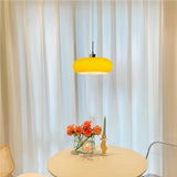 Yellow lit glass pendant light over a round table with sheer curtains