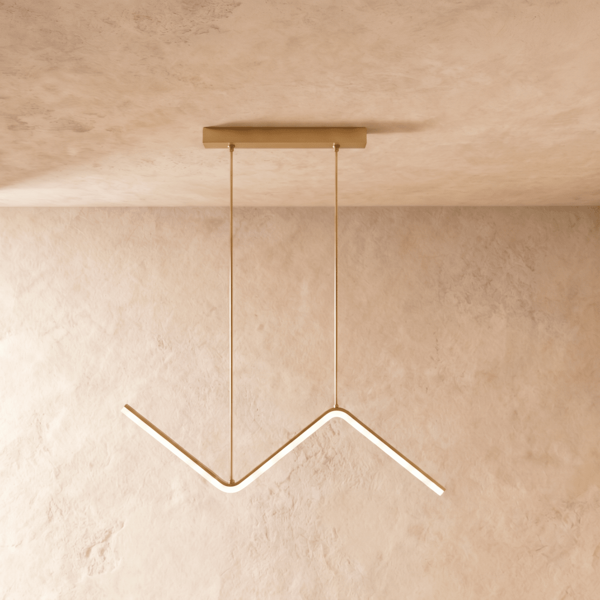 Gold zigzag pendant hanging from a brass ceiling plate against warm plaster