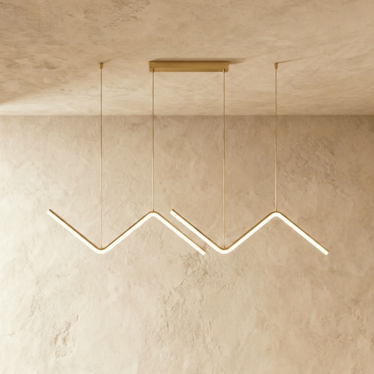 Row of gold zigzag pendant bars lit against a pale textured plaster wall