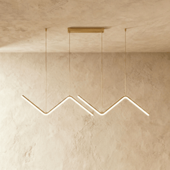Row of gold zigzag pendant bars lit against a pale textured plaster wall
